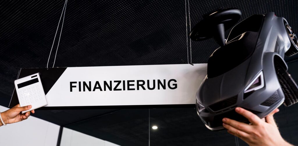 Auf dem Bild ist links eine Hand zu sehen die einen Taschenrechner hochhält, in der Mitte ist ein Schild auf dem Finanzierung steht und rechts davon ist eine Hand zu sehen die ein Spielzeug-Auto hochhält